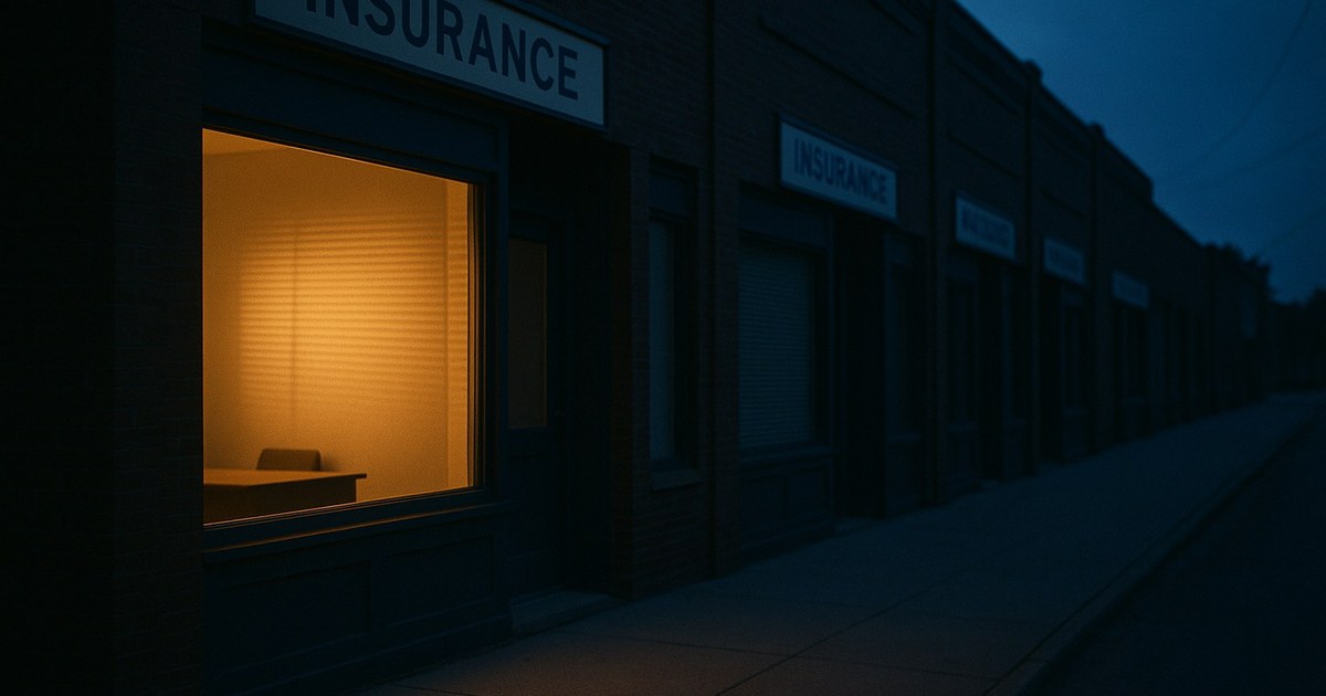 The agency office at dusk — desk lamp on, phone at rest, chairs squared for tomorrow