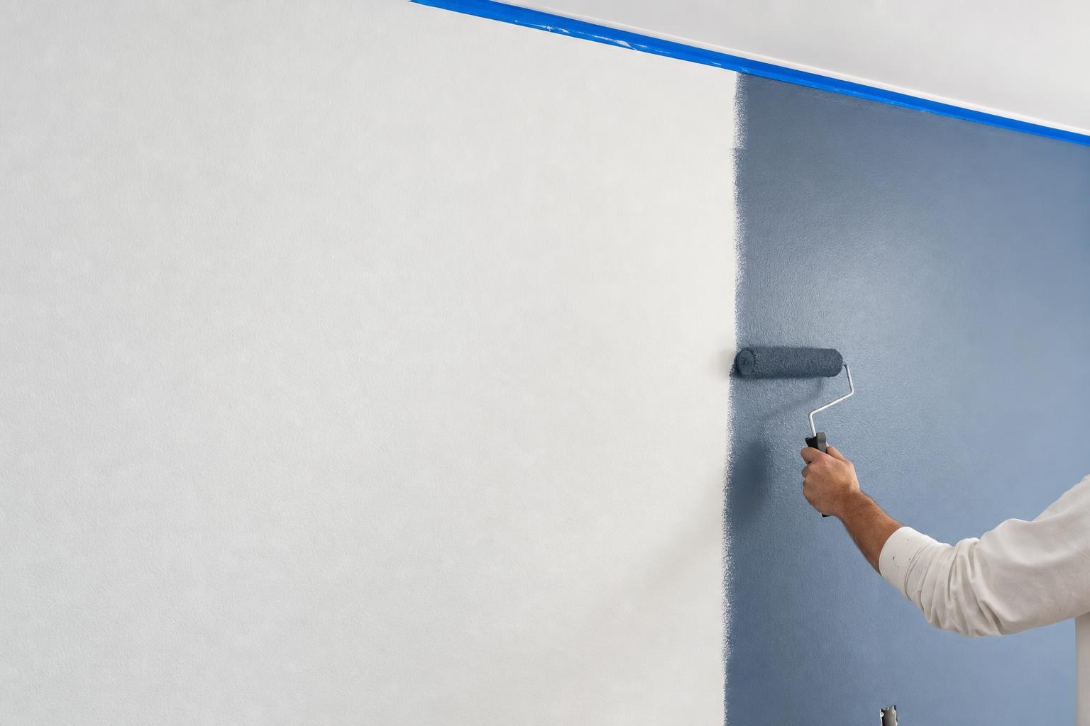 A painter on a ladder cutting in exterior trim on a bright morning
