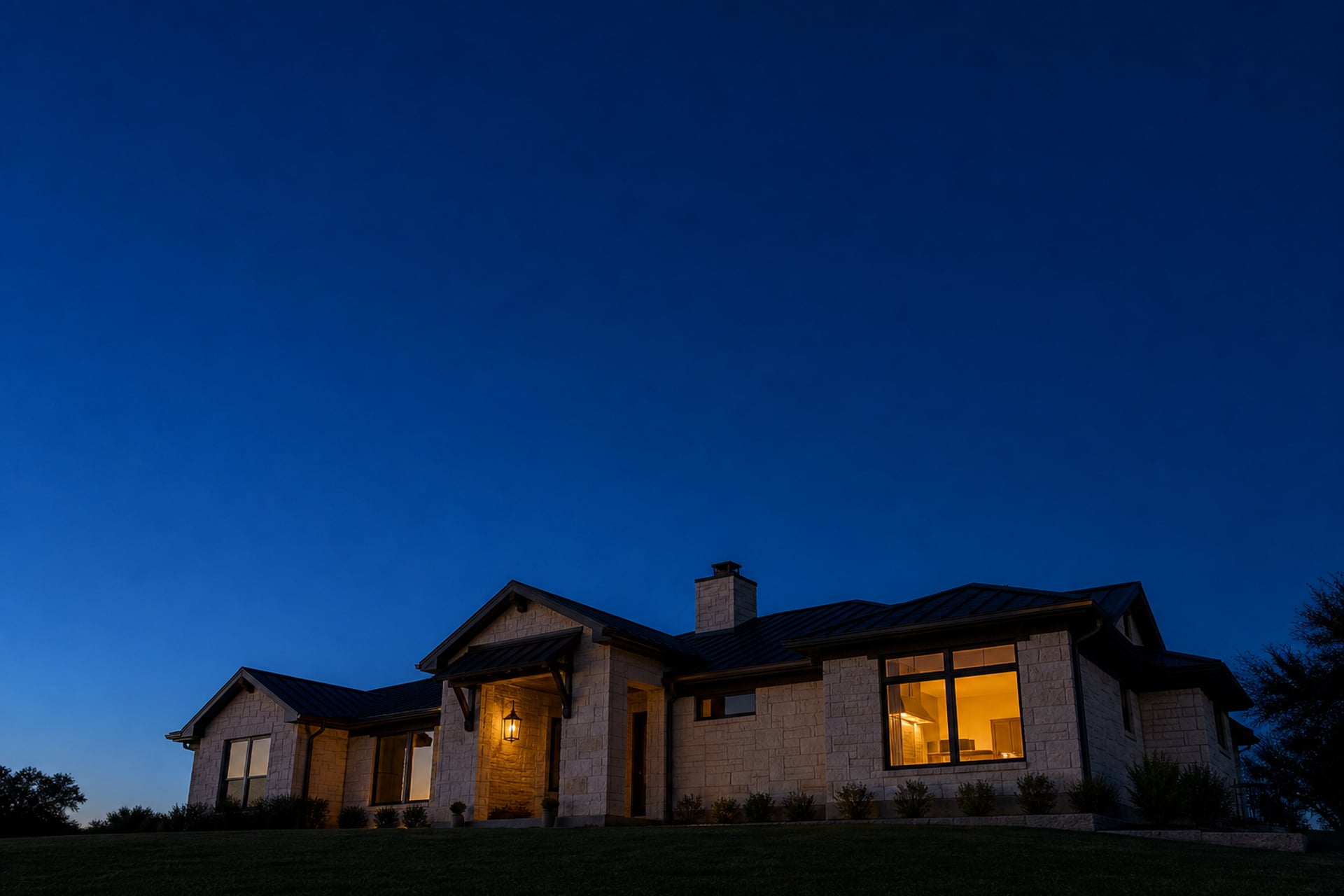 A limestone Texas home at blue-hour dusk, one kitchen window glowing — the hour the first roach shows up